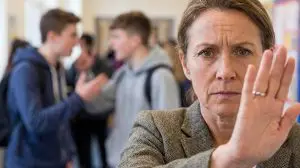 Stressed teacher standing in a corridor as two male pupils argue in the background