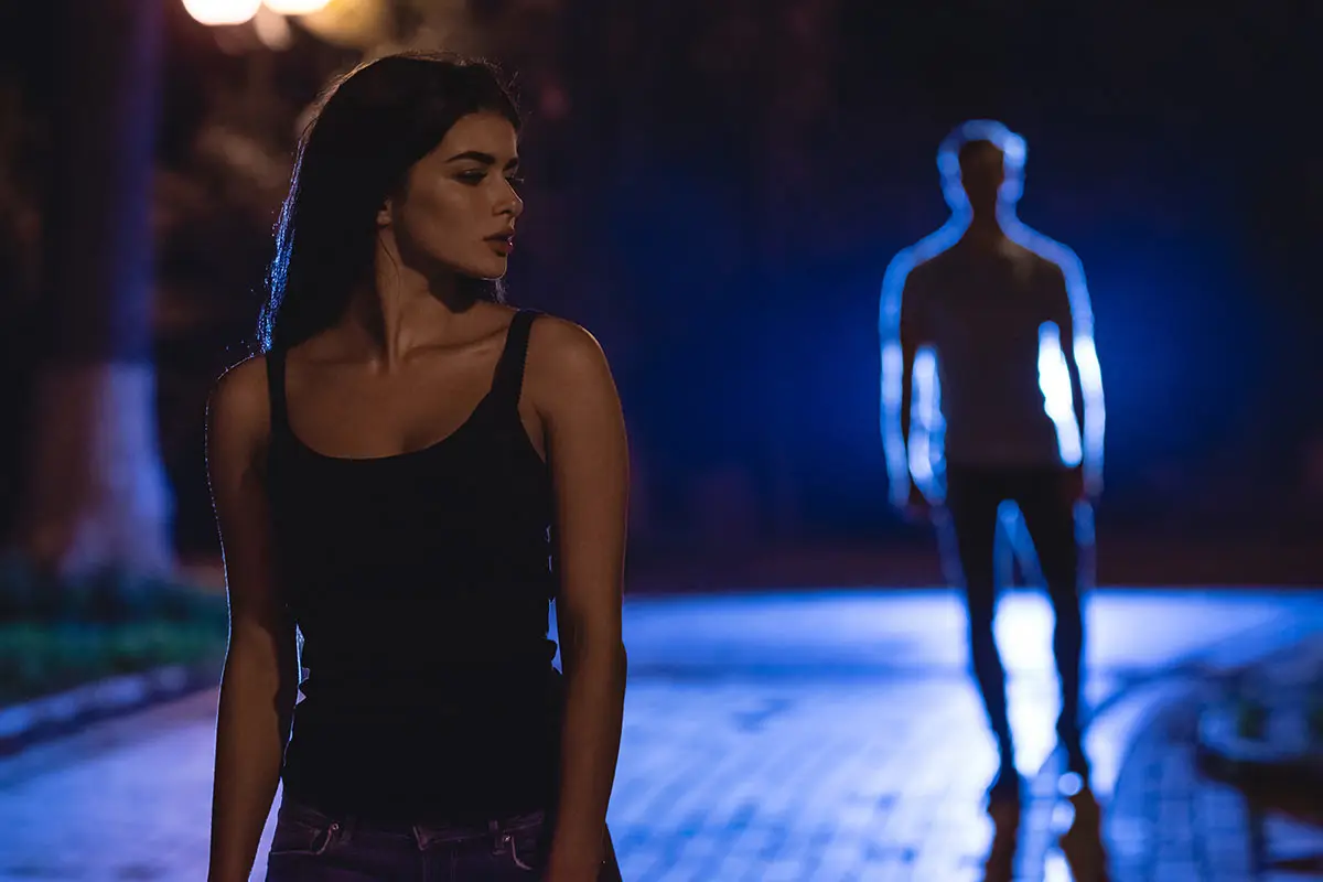 A lone female walking a dark street being followed by a male