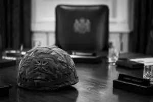 Black-and-white image of a British Army helmet resting on a Cabinet table with an empty chair behind it, symbolising defence leadership and political responsibility.